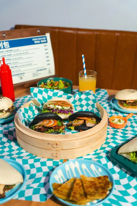 A table at Bao Bao with bao in a bamboo steamer, a cut scallion pancake, a salad and an orange juice, the menu card behind